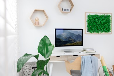 Green artificial plant wall panel and desk with computer in light room. Interior design