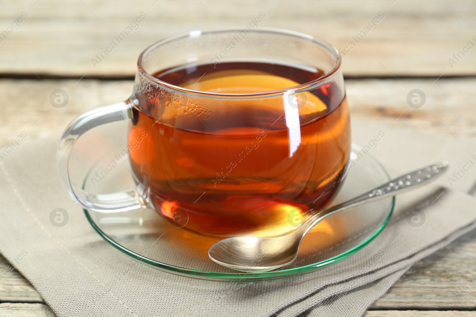 Photo of Aromatic tea in glass cup, spoon and napkin on wooden table