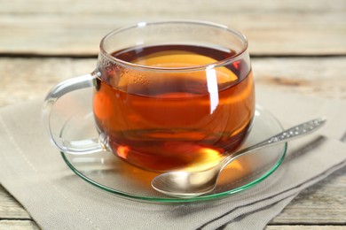 Aromatic tea in glass cup, spoon and napkin on wooden table