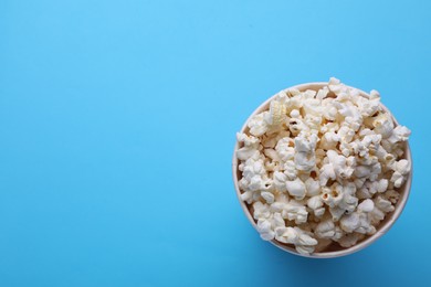Photo of Paper bucket with delicious popcorn on light blue background, top view. Space for text