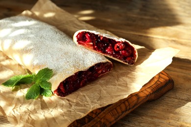 Photo of Delicious strudel with cherries, powdered sugar and mint on wooden table, closeup