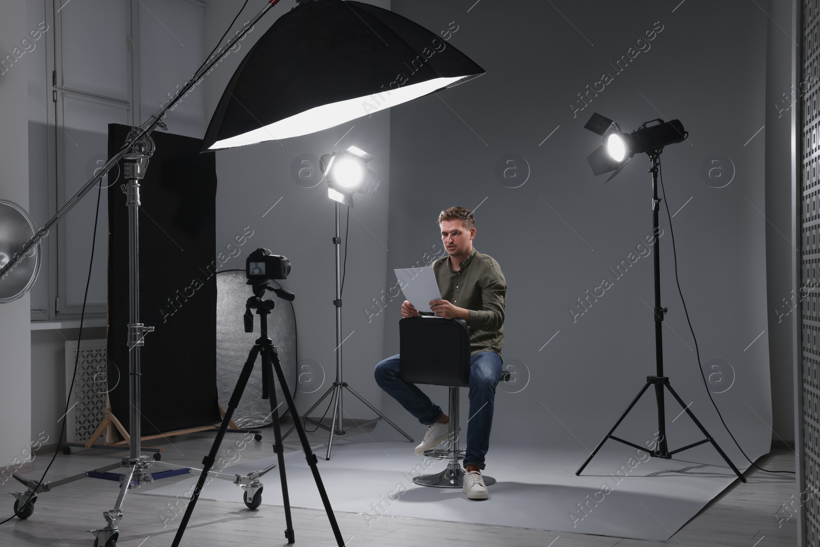 Photo of Casting call. Man with script sitting on chair and performing in front of camera in studio