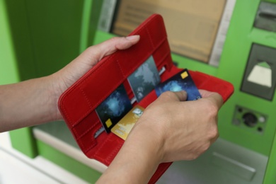 Mature woman with wallet and credit cards at modern cash machine, closeup