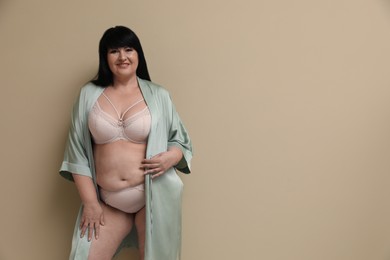 Photo of Beautiful overweight woman in sexy underwear and silk robe on beige background, space for text. Plus-size model