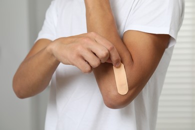 Man putting sticking plaster onto elbow indoors, closeup