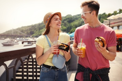Photo of Young happy couple with burgers walking on city street