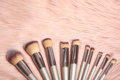 Photo of Set of professional makeup brushes on furry fabric, above view. Space for text