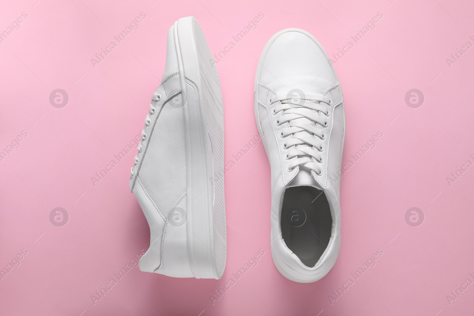 Photo of Pair of stylish white sneakers on pink background, top view