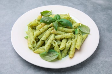 Photo of Delicious pasta with pesto sauce and basil on light grey table, closeup