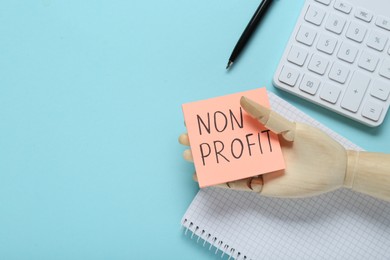 Non Profit concept. Flat lay composition with paper note in wooden mannequin hand on light blue background, space for text