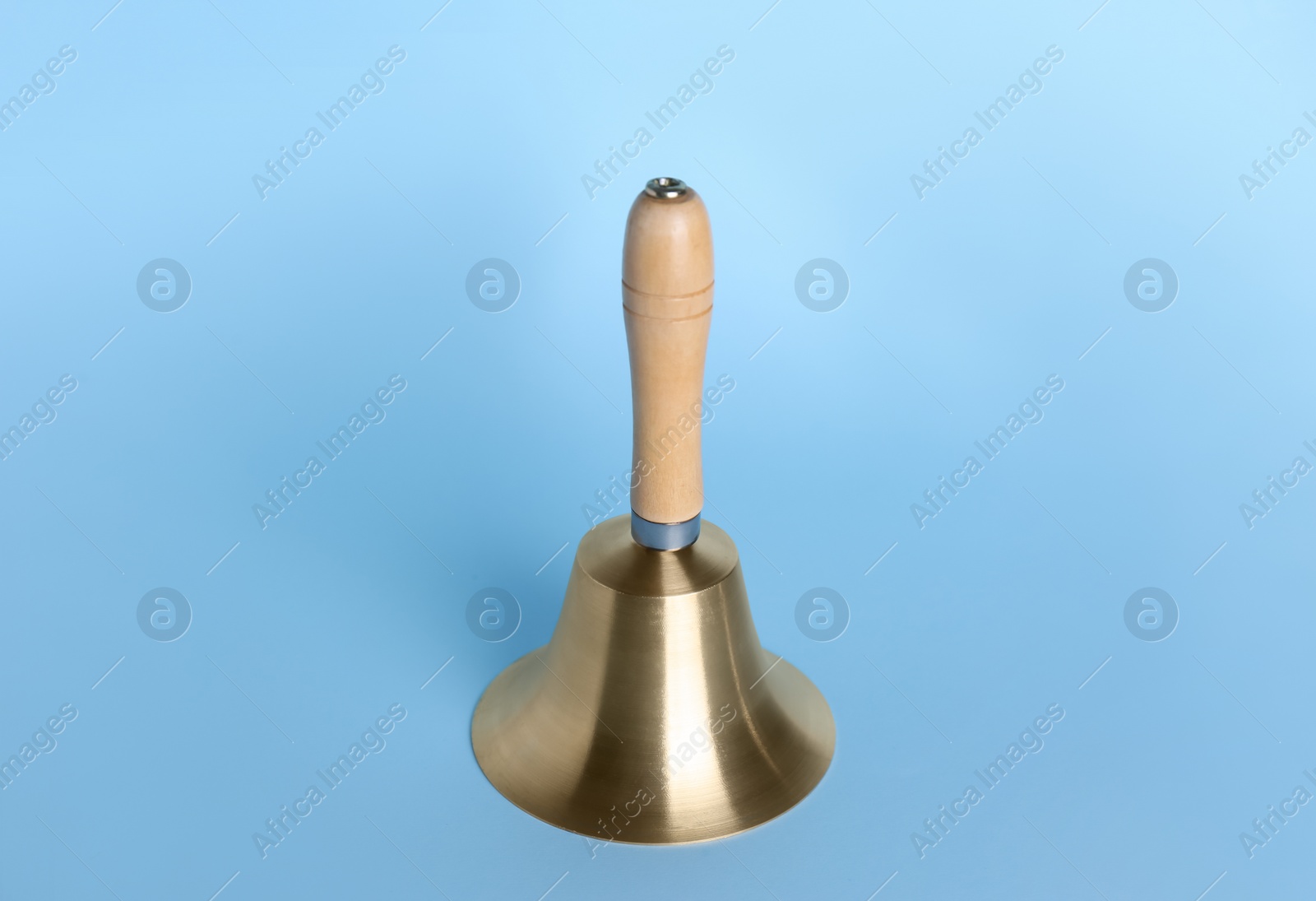 Photo of Golden school bell with wooden handle on light blue background