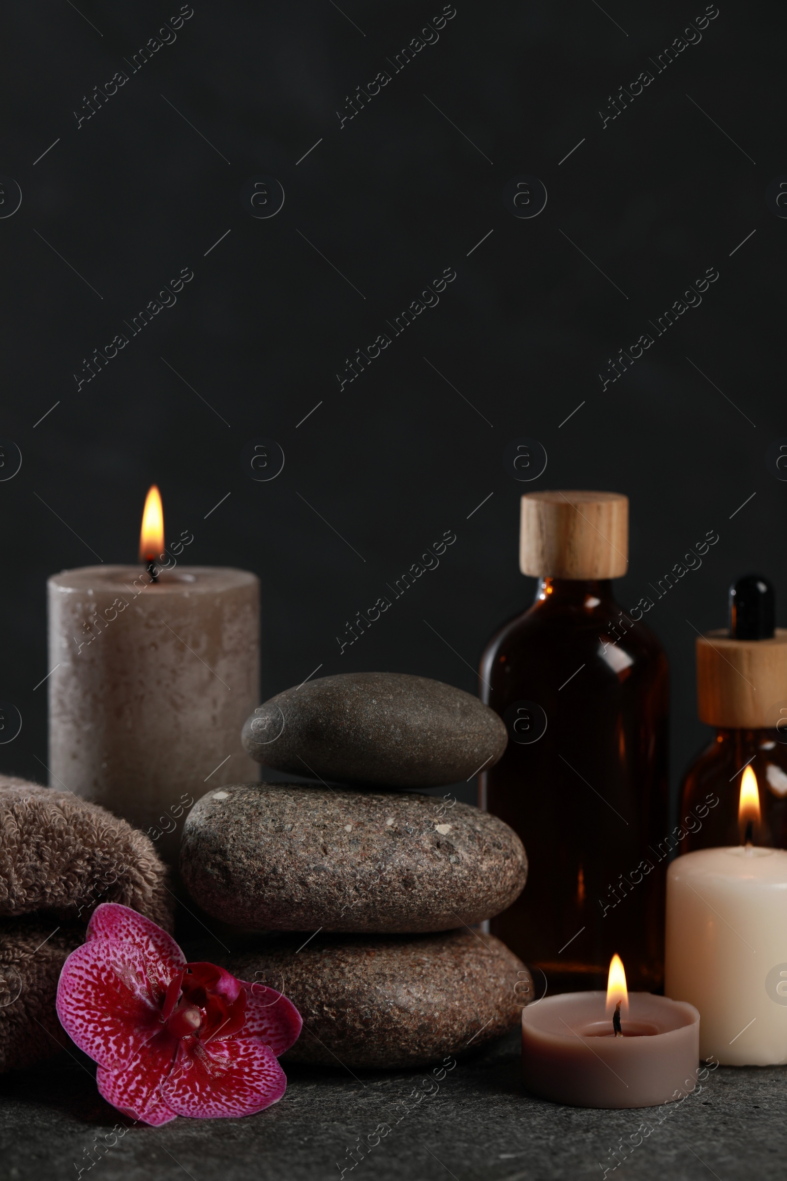 Photo of Beautiful composition with burning candles, spa stones and different care products on dark grey table