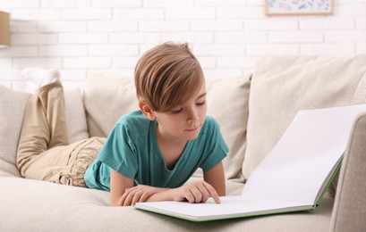 Photo of Little boy reading book on sofa at home