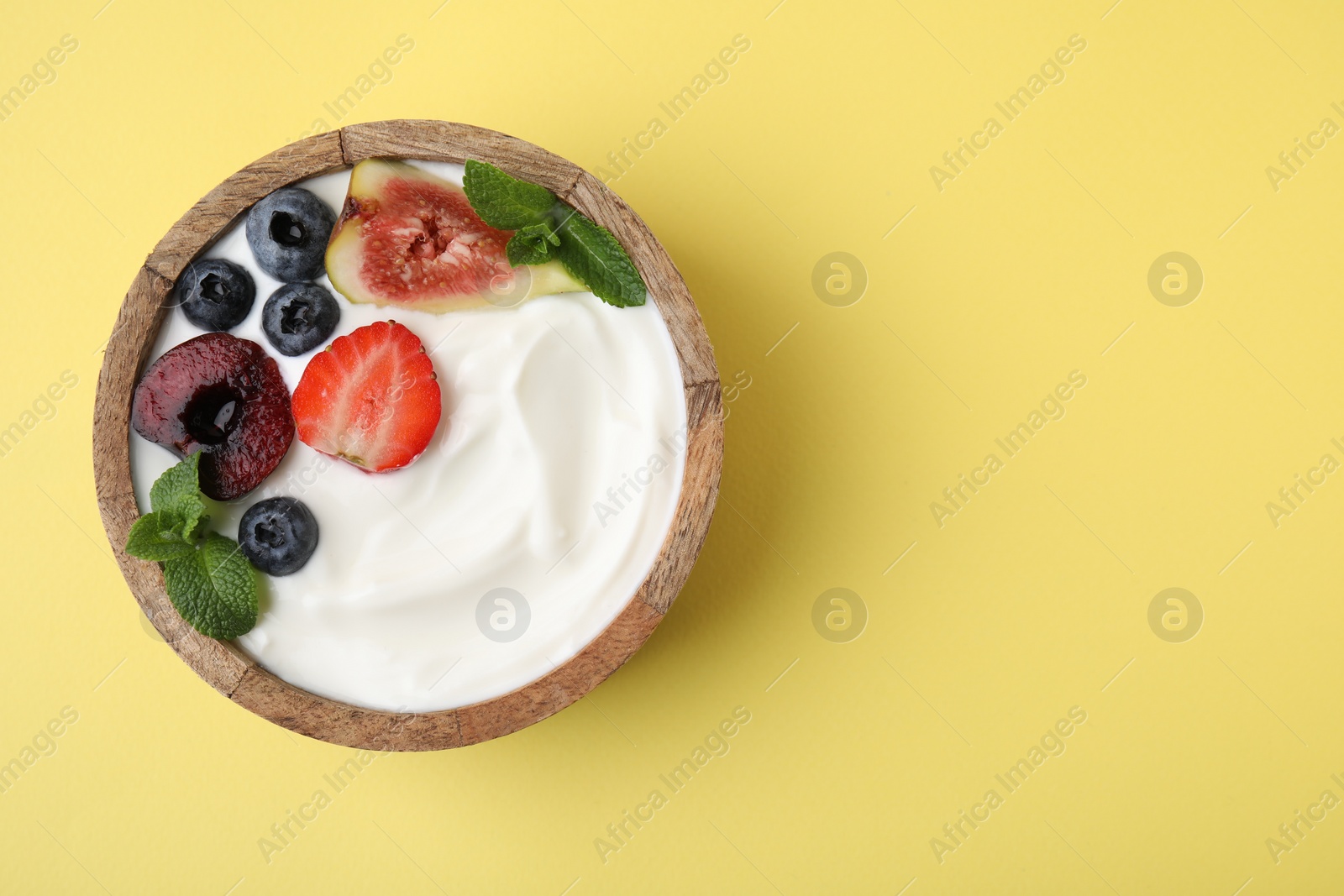 Photo of Bowl with yogurt, berries, fruits and mint on yellow background, top view. Space for text