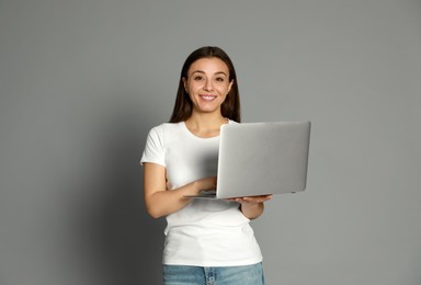 Photo of Young woman with modern laptop on grey background