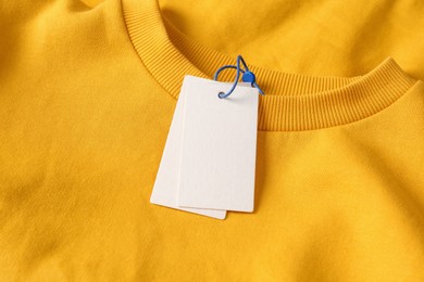 Photo of Blank white tags on yellow sweatshirt, top view. Space for text