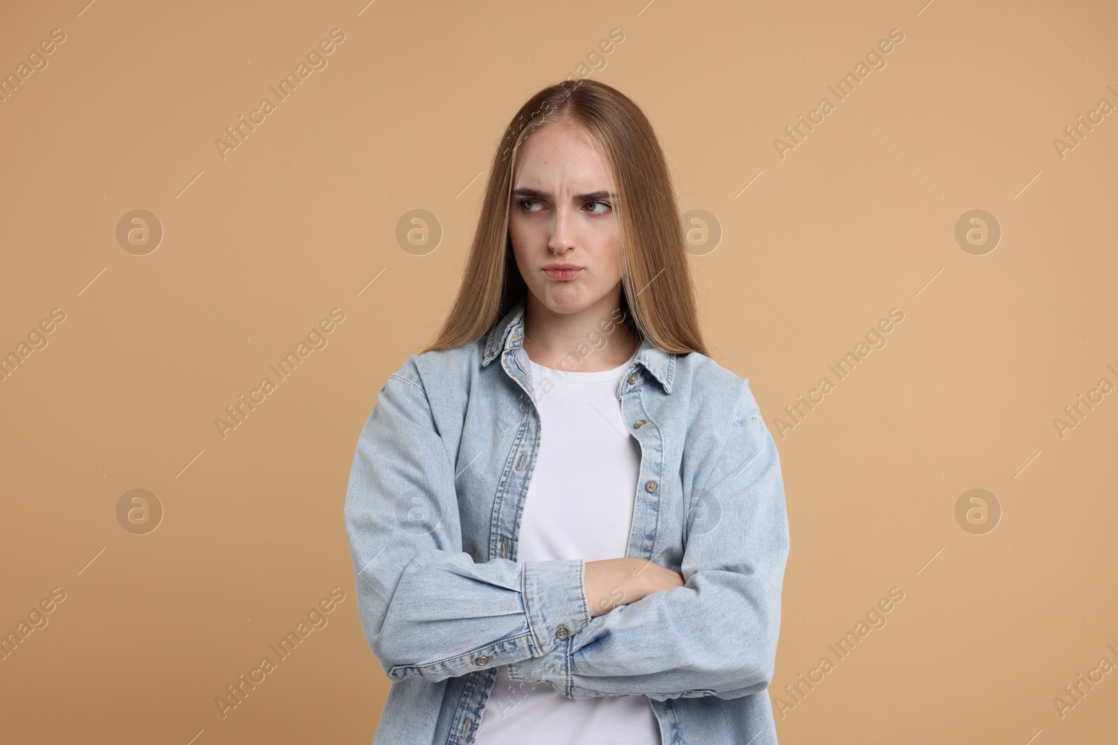 Photo of Resentful woman with crossed arms on beige background