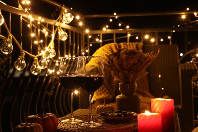 Glasses of wine, burning candles and decor on rattan table. Autumn evening on terrace