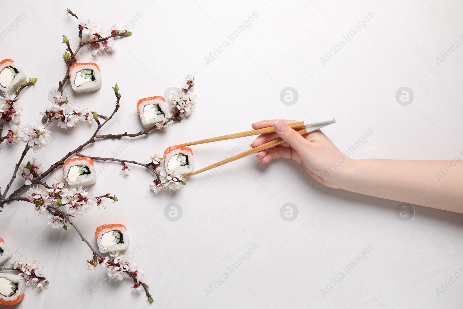 Photo of Woman taking tasty sushi roll with salmon at light table, top view