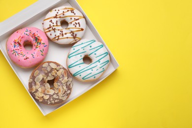 Photo of Box with tasty glazed donuts on yellow background, top view. Space for text
