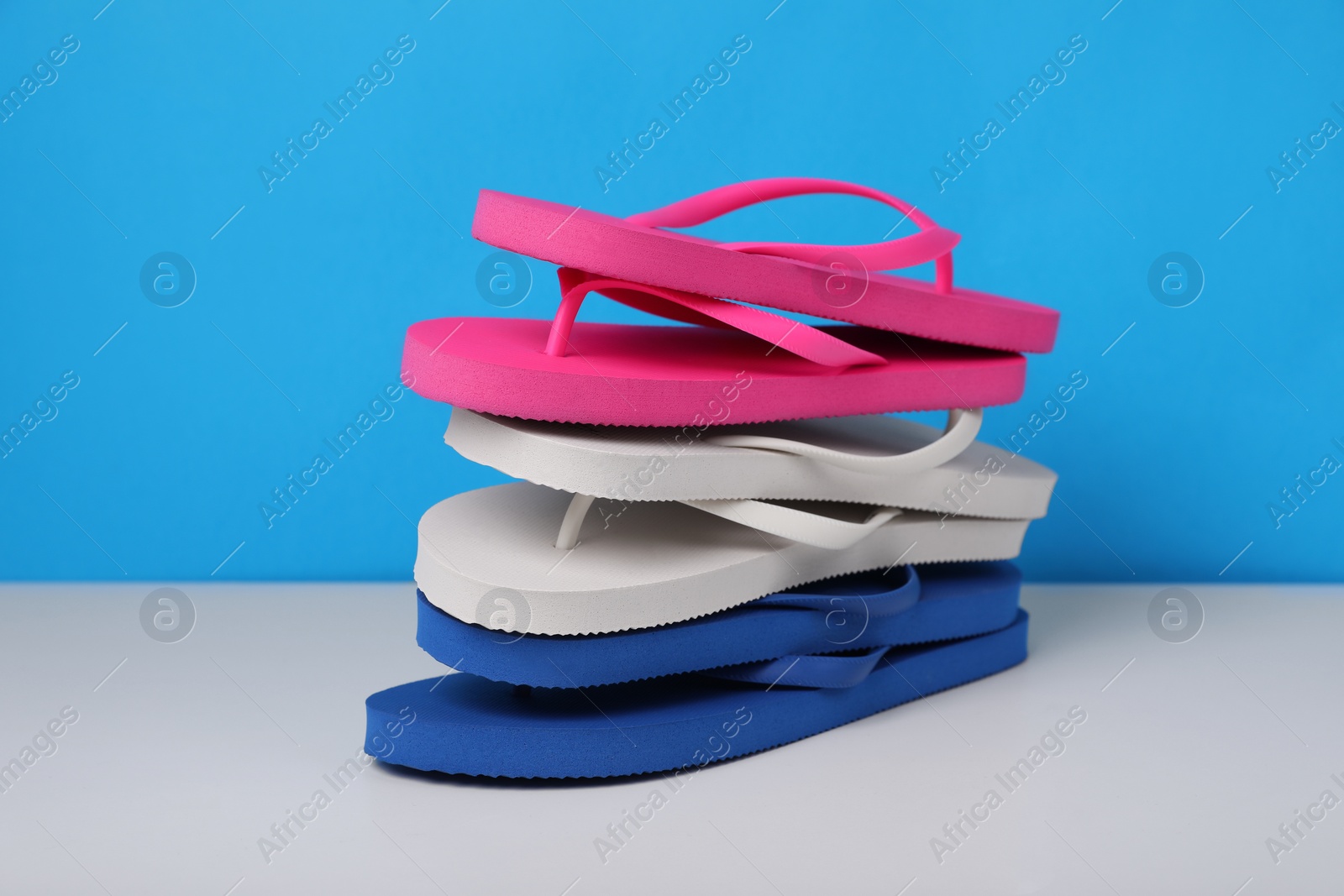 Photo of Stack of different flip flops on white table against light blue background