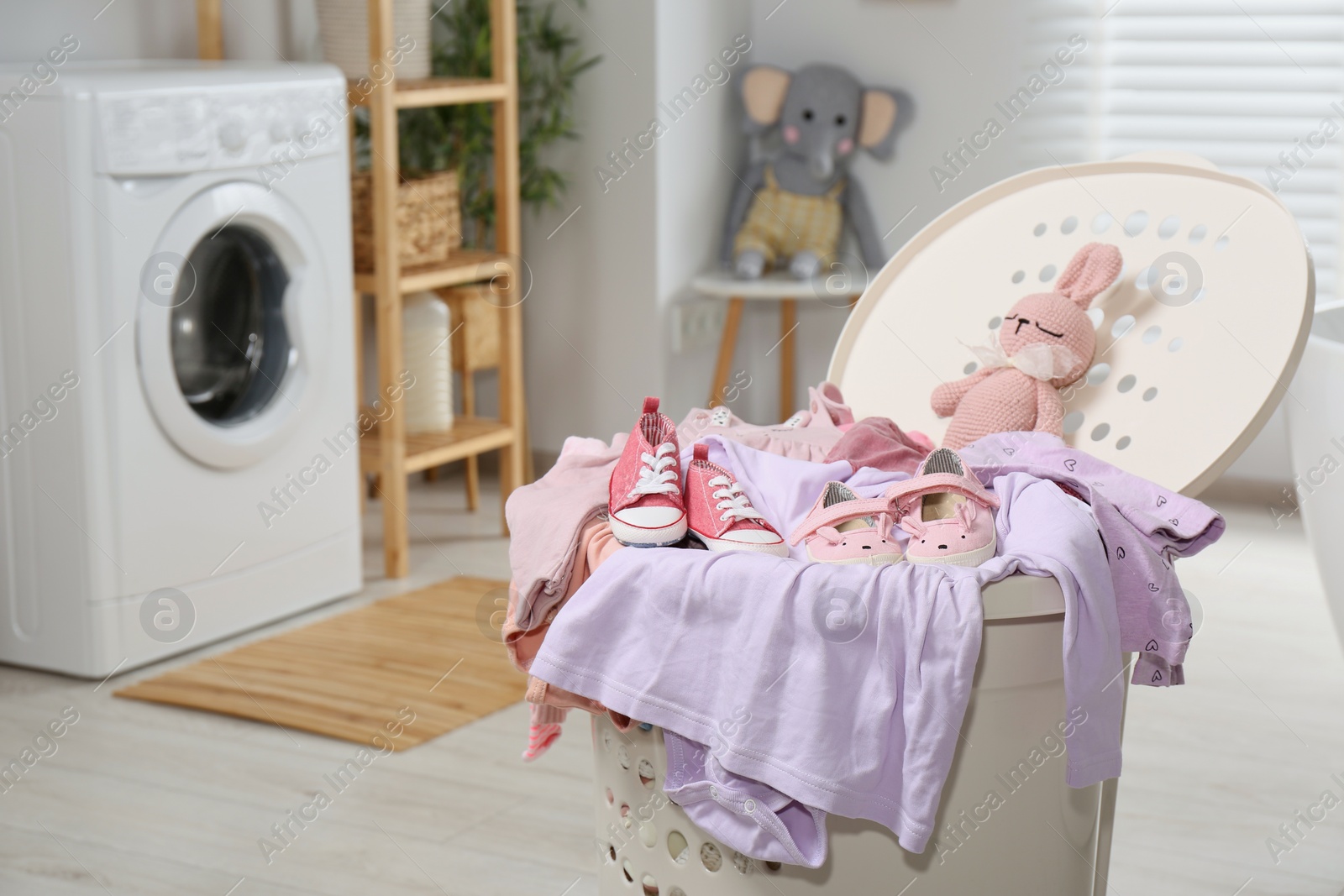 Photo of Laundry basket with baby clothes, shoes and crochet toy in bathroom