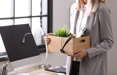 Photo of Young woman holding moving box with office stuff indoors, closeup