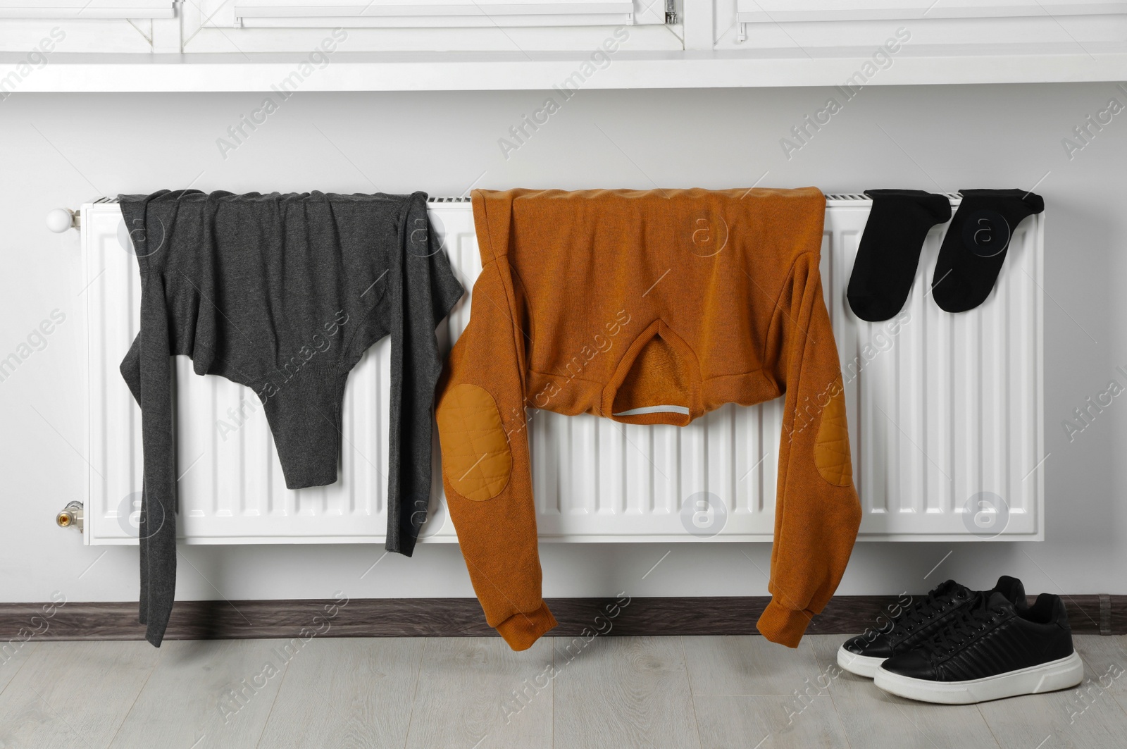 Photo of Heating radiator with clothes and shoes in room