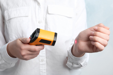 Photo of Woman measuring temperature with non contact infrared thermometer on light background, closeup