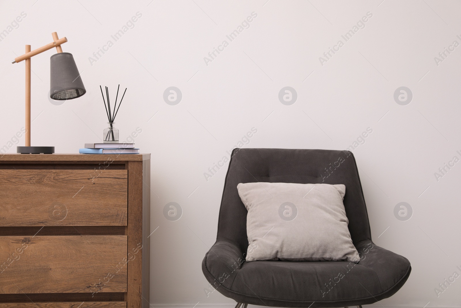 Photo of Modern chest of drawers and armchair near white wall in room