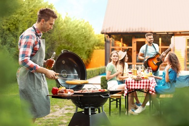 Photo of Group of friends at barbecue party outdoors. Young man near grill