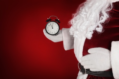 Photo of Santa Claus holding alarm clock on red background, space for text. Christmas countdown