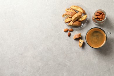 Slices of tasty cantucci, aromatic coffee and nuts on light grey table, flat lay with space for text. Traditional Italian almond biscuits