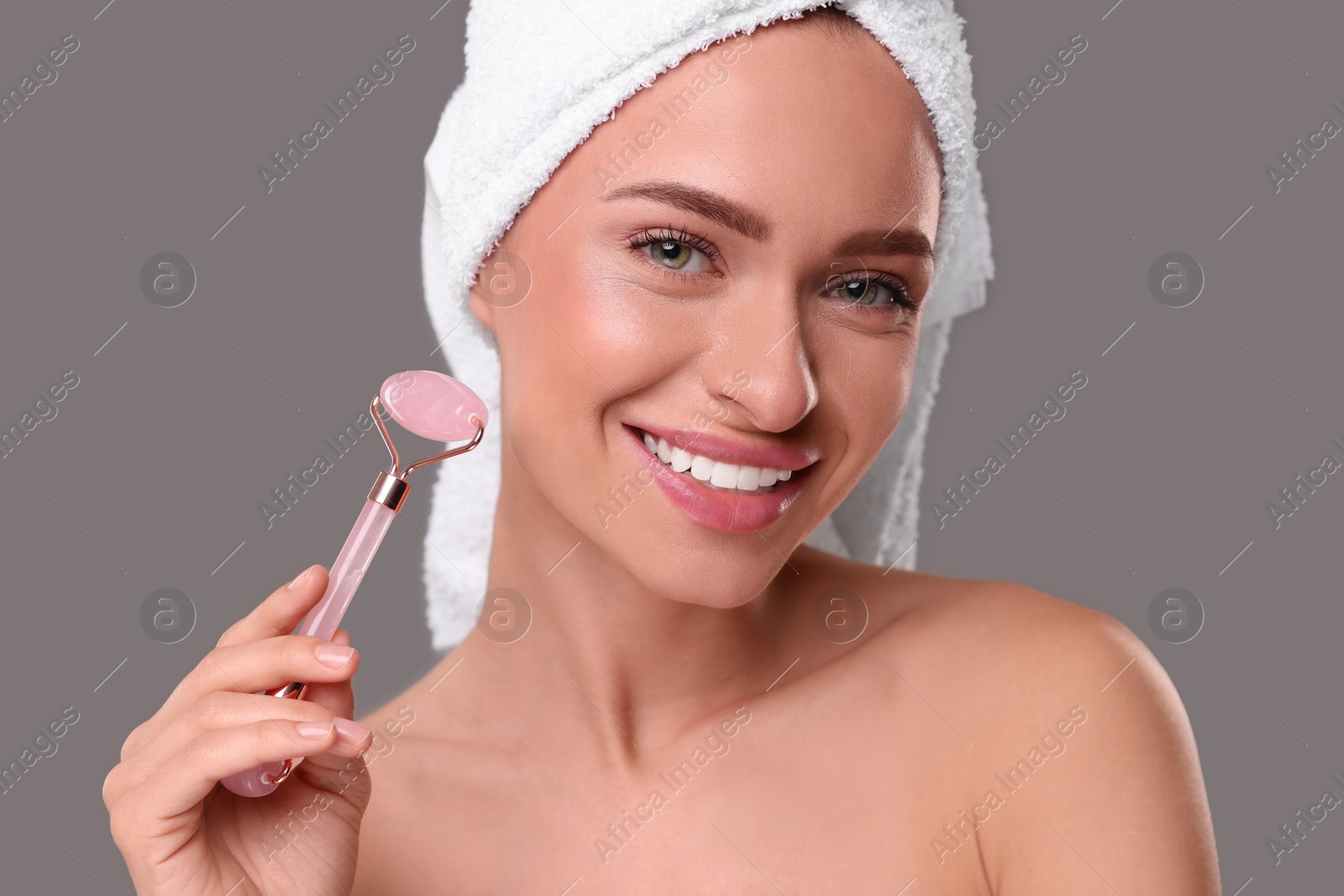 Photo of Young woman with rose quartz roller on grey background. Facial massage