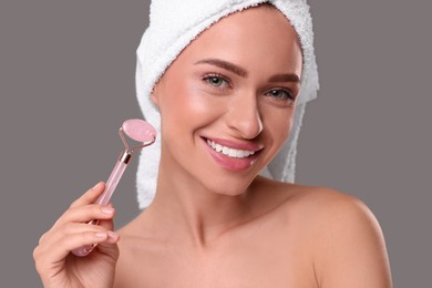 Photo of Young woman with rose quartz roller on grey background. Facial massage