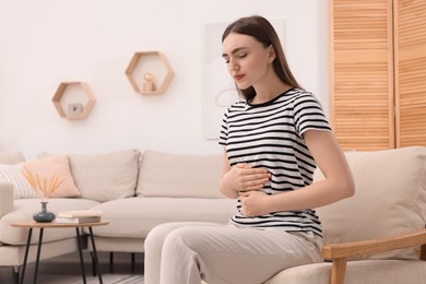 Photo of Young woman suffering from stomach pain at home. Space for text