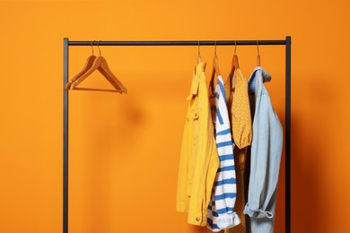 Rack with stylish clothes on wooden hangers against orange background