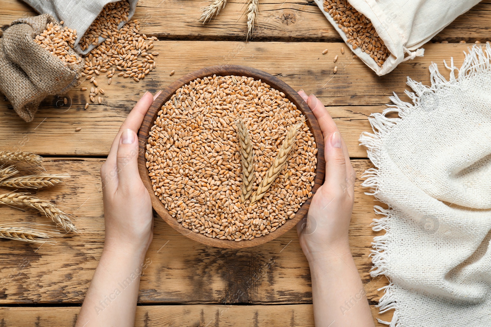 Photo of Woman holding bowl of wheat grains at wooden table, top view