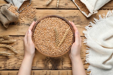 Photo of Woman holding bowl of wheat grains at wooden table, top view