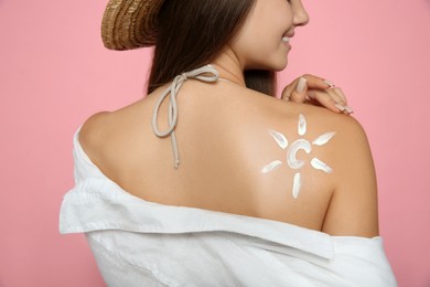 Teenage girl with sun protection cream on her back against pink background, closeup