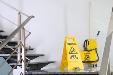 Safety sign with phrase Caution wet floor and mop bucket on stairs. Cleaning service