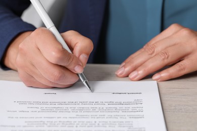 Woman signing document at light wooden table, closeup