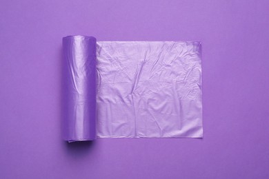 Photo of Roll of color garbage bags on violet background, top view