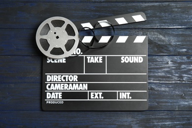 Photo of Clapperboard and reel on wooden background, top view. Cinema production