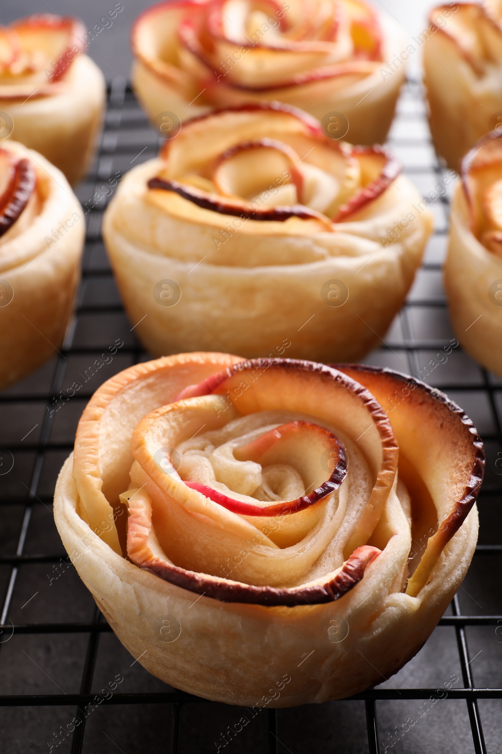 Photo of Cooling rack with freshly baked apple roses on grey table, closeup. Beautiful dessert