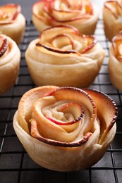 Photo of Cooling rack with freshly baked apple roses on grey table, closeup. Beautiful dessert