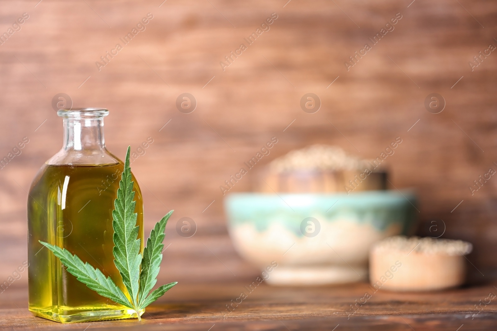 Photo of Bottle with hemp oil and fresh leaf on wooden table. Space for text