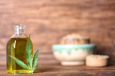 Bottle with hemp oil and fresh leaf on wooden table. Space for text