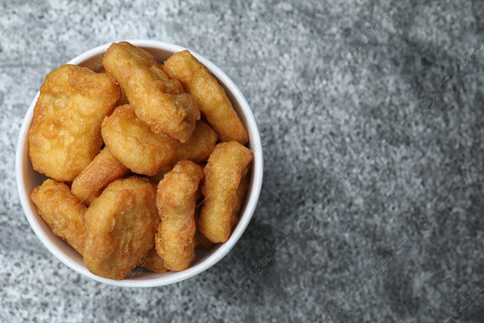 Photo of Bucket with tasty chicken nuggets on grey table, top view. Space for text