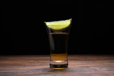 Photo of Mexican Tequila shot with lime slice on wooden table against black background